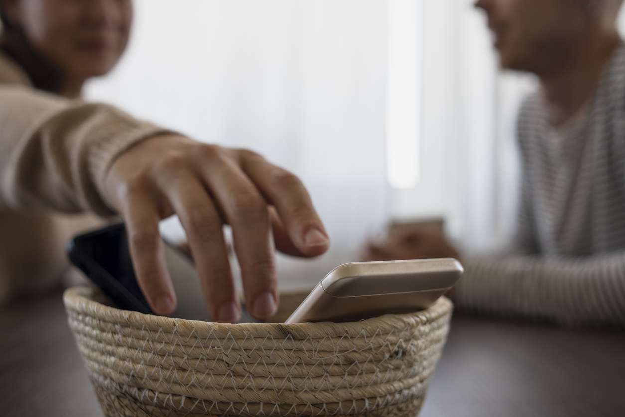 People on meeting without their phones. Digital detox concept. Turned off phones putting in basket
