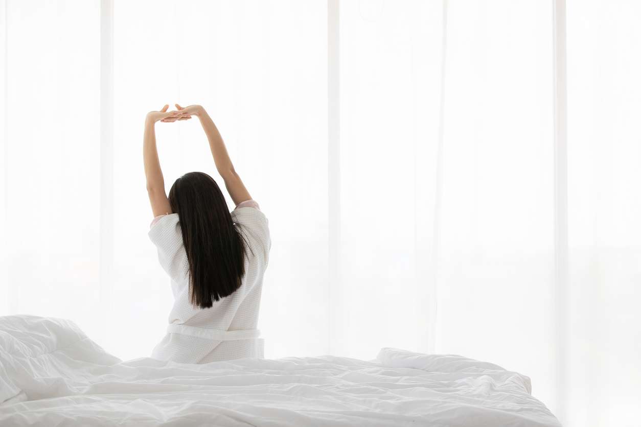 Back of woman on bed in the morning, stretching hands and body. Concept for start new day with happiness. Copyspace on the right.